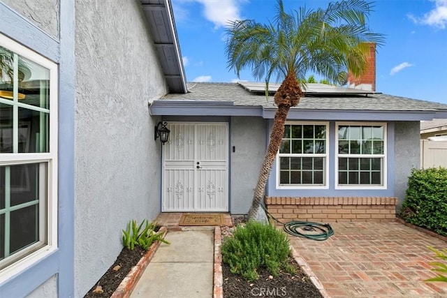 doorway to property with brick siding, roof mounted solar panels, and stucco siding