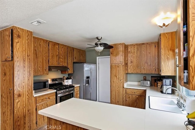 kitchen with appliances with stainless steel finishes, a sink, a peninsula, under cabinet range hood, and visible vents