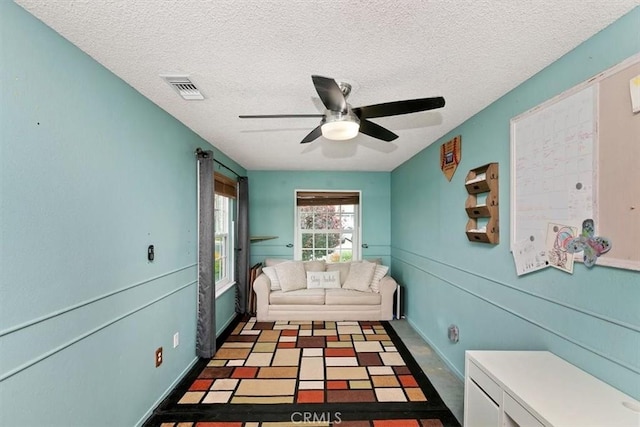 living area with a ceiling fan, a textured ceiling, and visible vents