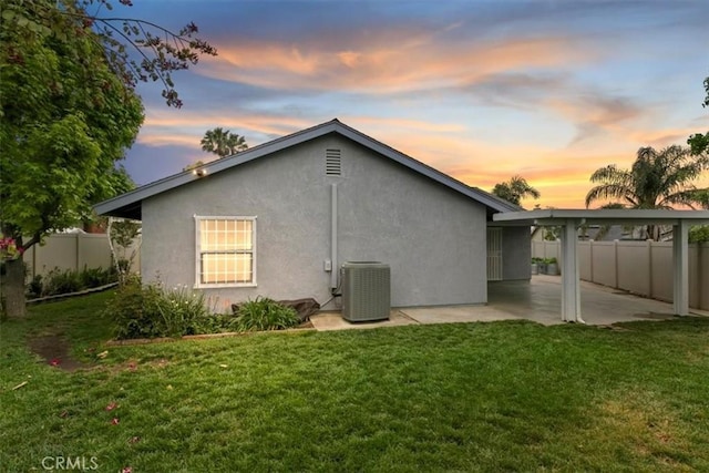 rear view of house with central AC, fence, stucco siding, a patio area, and a yard