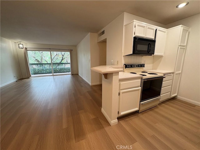 kitchen featuring visible vents, wood finished floors, black microwave, white range with electric cooktop, and tasteful backsplash