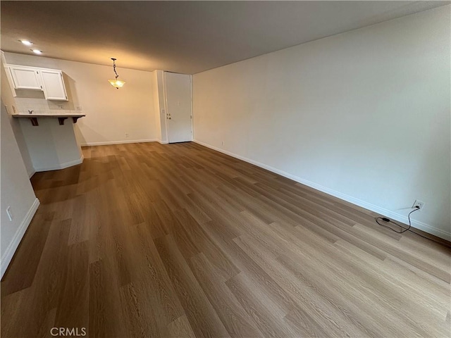 unfurnished living room with dark wood-type flooring and baseboards