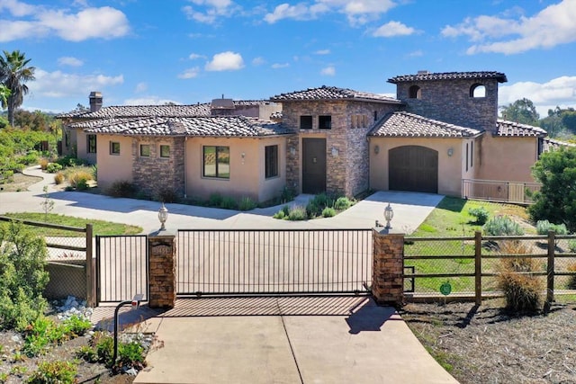 mediterranean / spanish house featuring a tiled roof, driveway, a fenced front yard, a garage, and stucco siding