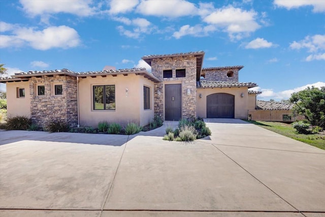 mediterranean / spanish-style house with driveway, a tile roof, stone siding, and stucco siding