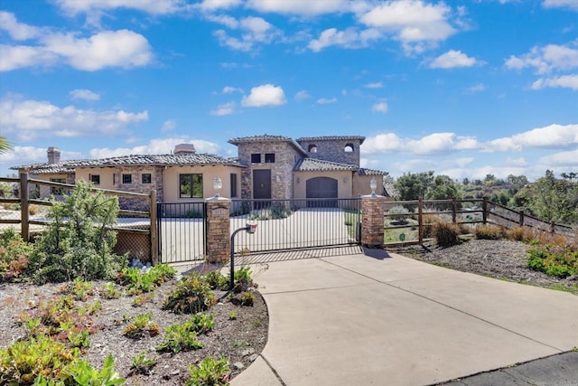 mediterranean / spanish-style house featuring stone siding, stucco siding, a gate, a fenced front yard, and a tile roof