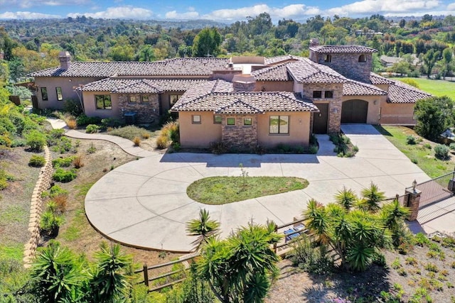 mediterranean / spanish-style home with a chimney, a tile roof, fence, curved driveway, and stucco siding