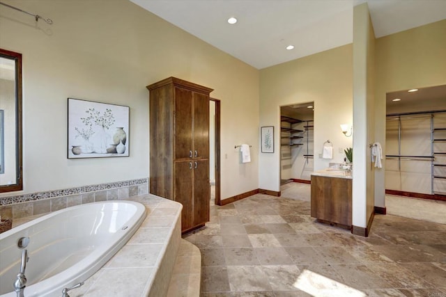 full bathroom featuring a walk in closet, a bath, vanity, baseboards, and recessed lighting