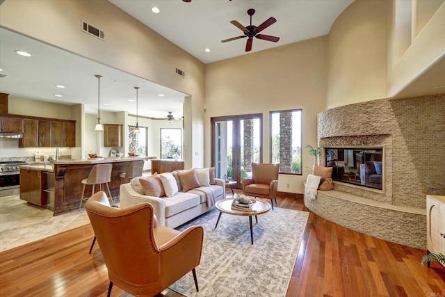 living room with a towering ceiling, a ceiling fan, visible vents, and light wood-type flooring