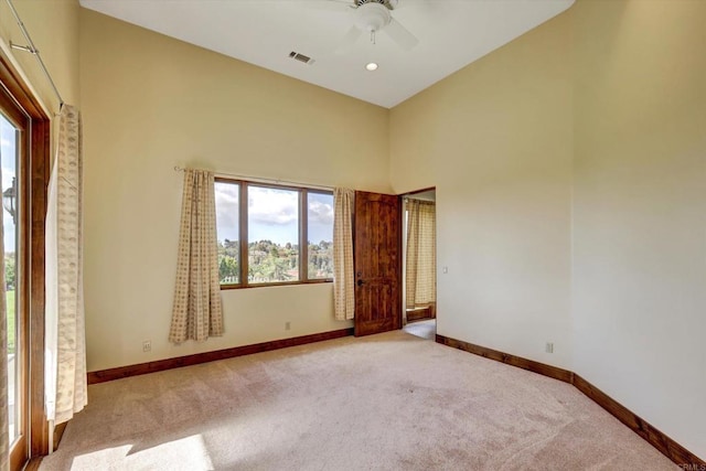 spare room featuring visible vents, baseboards, ceiling fan, a high ceiling, and carpet flooring