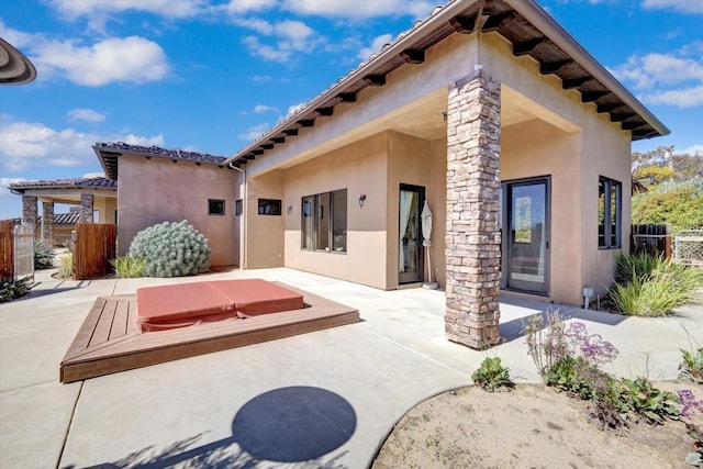 back of property featuring a covered hot tub, stucco siding, and a patio area