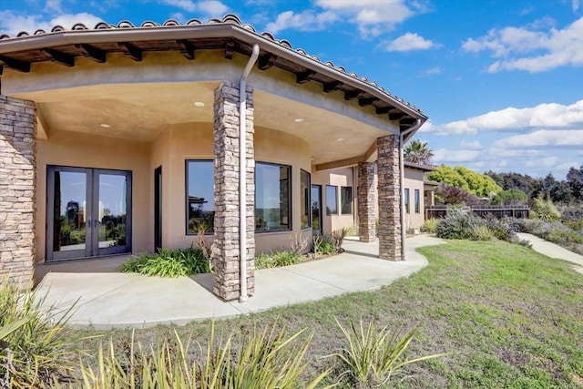 exterior space featuring a lawn, stucco siding, french doors, and stone siding
