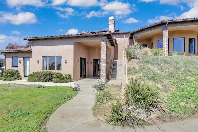 view of front of home featuring a chimney, stucco siding, and a front yard