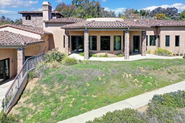 back of house featuring a yard, a chimney, a tile roof, and stucco siding