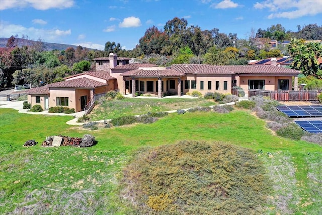 view of front of property featuring a front lawn, stucco siding, a tiled roof, and a chimney