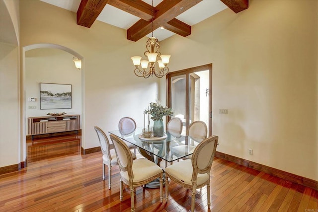 dining area with baseboards, arched walkways, light wood-style flooring, and beam ceiling