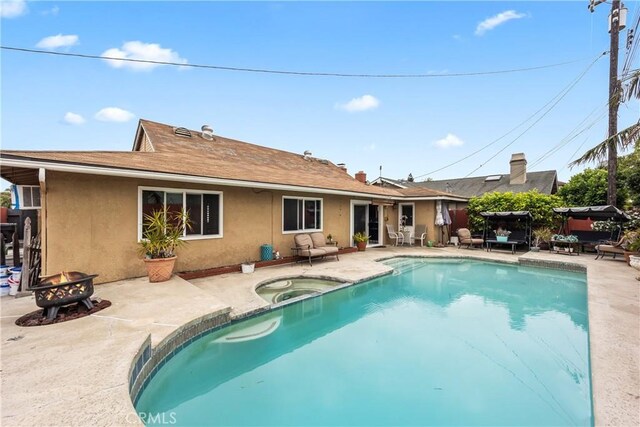 14901 Quill Cir, Huntington Beach, CA 92647 - rear view of property featuring an in-ground hot tub, stucco siding, a fire pit, and a patio