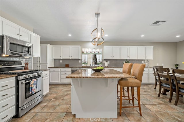 kitchen featuring visible vents, a kitchen island, light stone countertops, tasteful backsplash, and stainless steel appliances