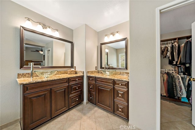 full bathroom with tile patterned flooring, ceiling fan, a walk in closet, two vanities, and a sink
