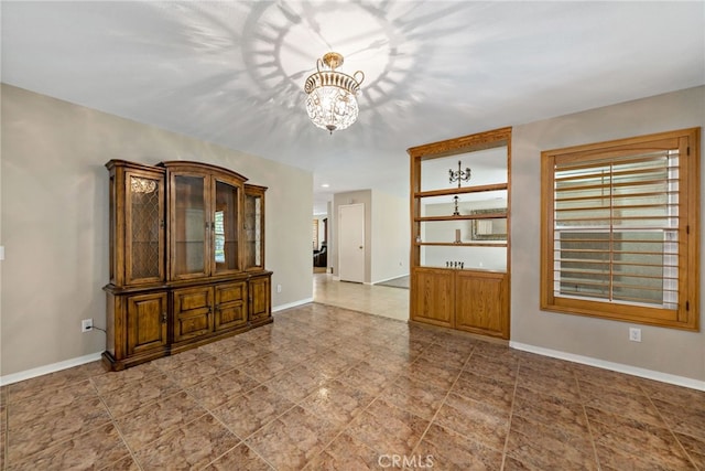 tiled empty room featuring an inviting chandelier and baseboards