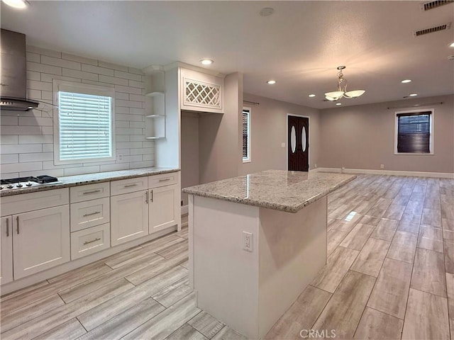 kitchen with white cabinets, wood finish floors, light stone counters, wall chimney exhaust hood, and stainless steel gas stovetop