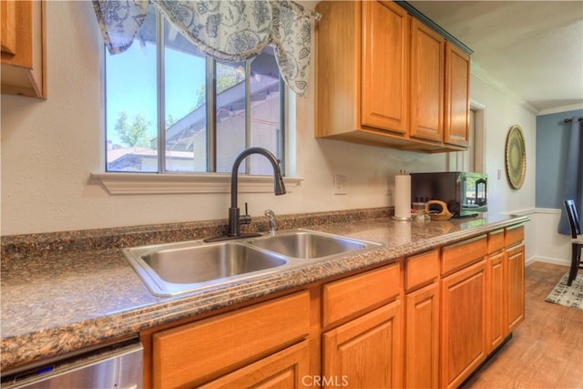 kitchen with crown molding, dark countertops, stainless steel dishwasher, a sink, and light wood finished floors