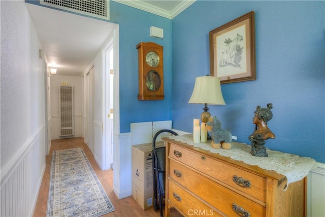 hallway featuring visible vents, a wainscoted wall, light wood finished floors, a decorative wall, and a heating unit