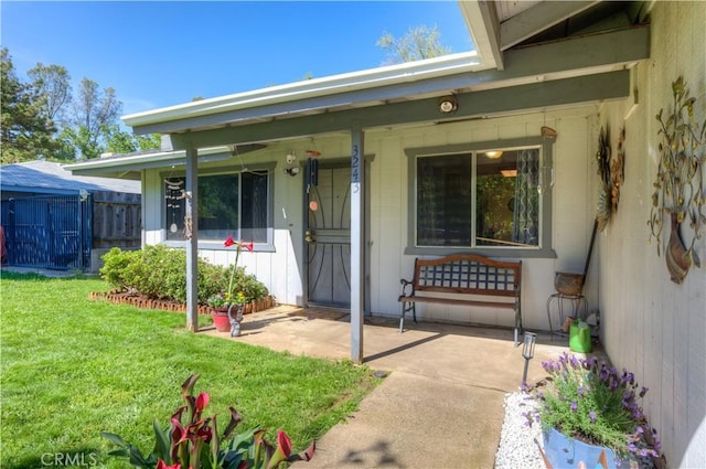 view of exterior entry with a lawn, fence, and a porch