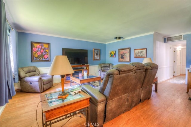 living area with visible vents, ornamental molding, light wood finished floors, and a wainscoted wall