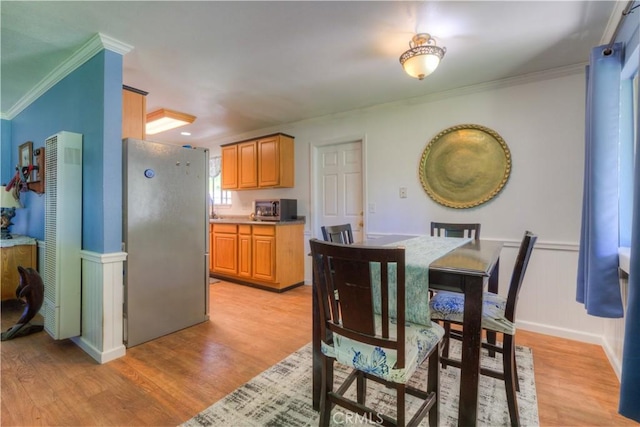 dining area with light wood-style floors, crown molding, and wainscoting