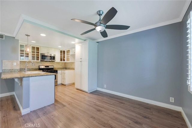 kitchen with stainless steel appliances, a sink, a peninsula, backsplash, and light stone countertops