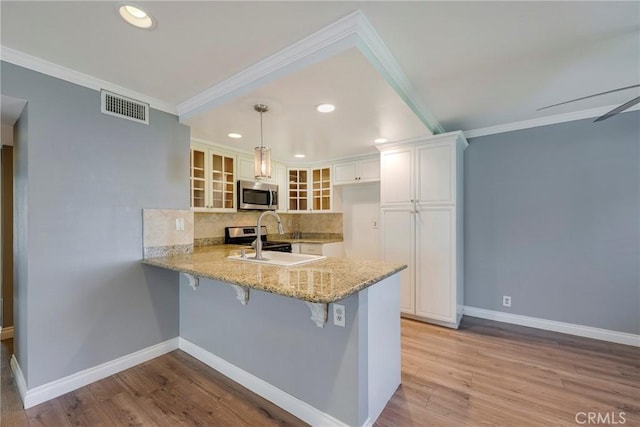 kitchen with stainless steel appliances, a peninsula, glass insert cabinets, decorative backsplash, and light stone countertops