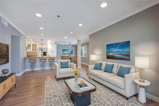 living room with crown molding, recessed lighting, light wood-style floors, baseboards, and a ceiling fan