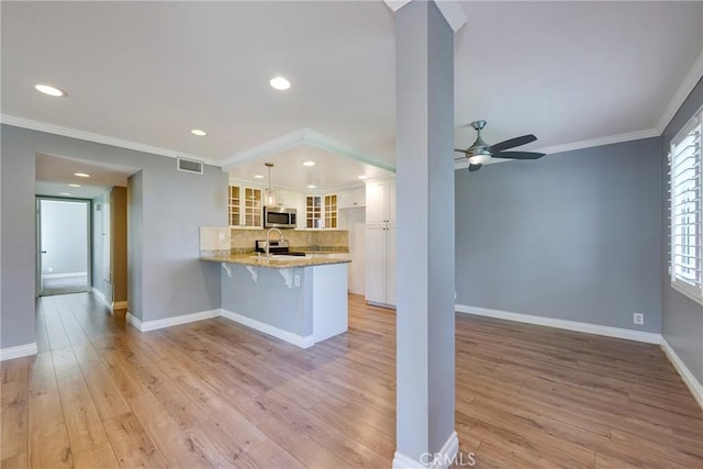 kitchen featuring stainless steel microwave, a peninsula, glass insert cabinets, white cabinets, and light stone counters