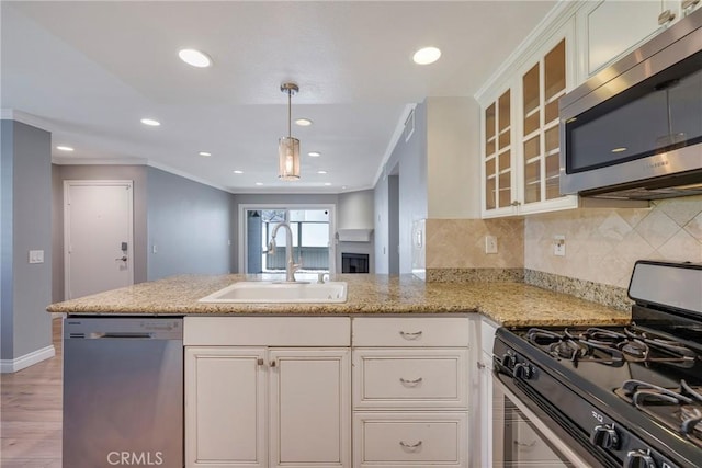 kitchen with stainless steel appliances, a sink, crown molding, a peninsula, and white cabinetry