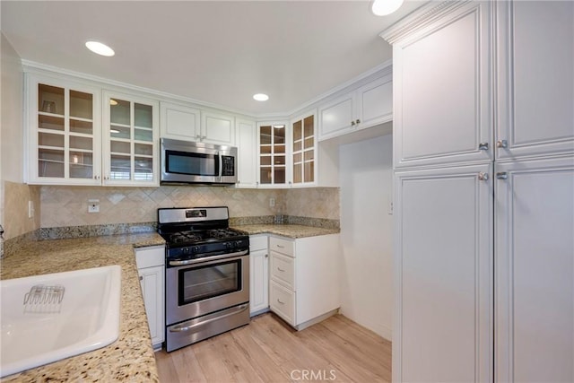 kitchen featuring stainless steel appliances, a sink, light wood-style floors, white cabinetry, and decorative backsplash
