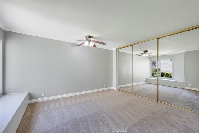 unfurnished bedroom featuring carpet flooring, baseboards, ceiling fan, crown molding, and a closet