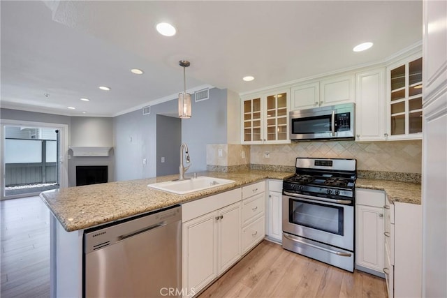 kitchen featuring appliances with stainless steel finishes, a sink, a peninsula, light wood-type flooring, and white cabinetry