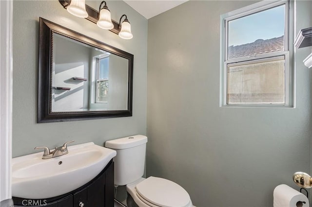 half bathroom featuring toilet, a healthy amount of sunlight, and vanity