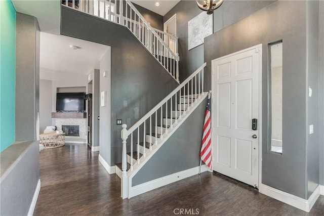 foyer featuring a fireplace, stairs, baseboards, wood finished floors, and a towering ceiling