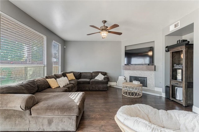 living room featuring ceiling fan, visible vents, dark wood finished floors, baseboards, and a glass covered fireplace
