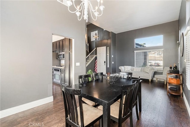 dining room with dark wood-type flooring, baseboards, a towering ceiling, and a chandelier
