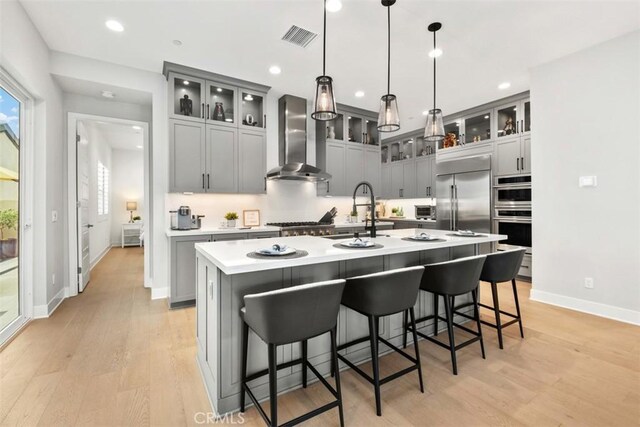 297 Sawbuck, Irvine, CA 92618 - kitchen featuring wall chimney range hood, stainless steel appliances, a sink, baseboards, and light wood-type flooring