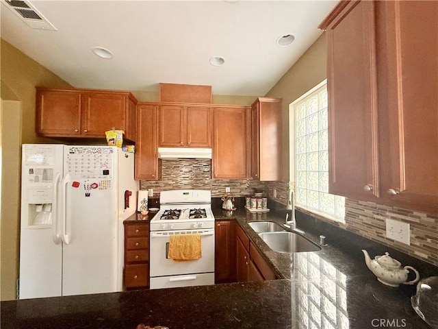7163 Watcher St, Commerce, CA 90040 - kitchen with white appliances, a sink, under cabinet range hood, decorative backsplash, and dark stone counters