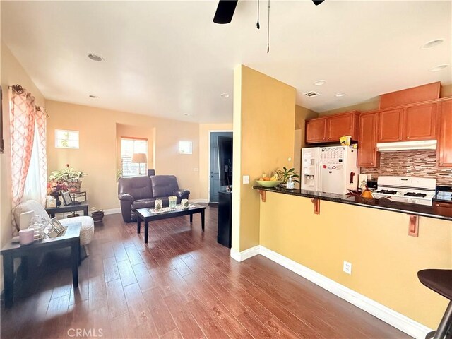 7163 Watcher St, Commerce, CA 90040 - kitchen featuring white appliances, under cabinet range hood, a ceiling fan, decorative backsplash, and dark countertops