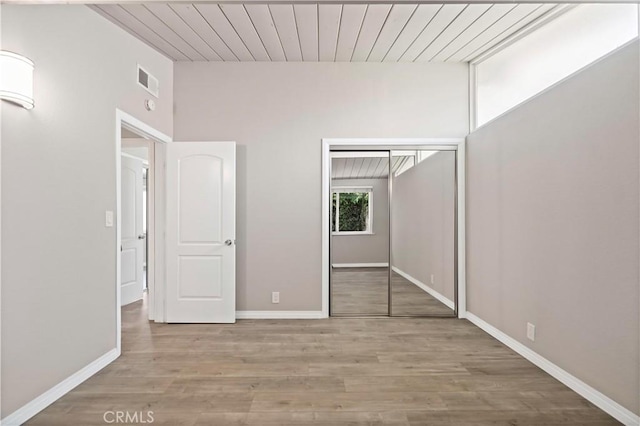 unfurnished bedroom with a closet, baseboards, wood finished floors, and visible vents