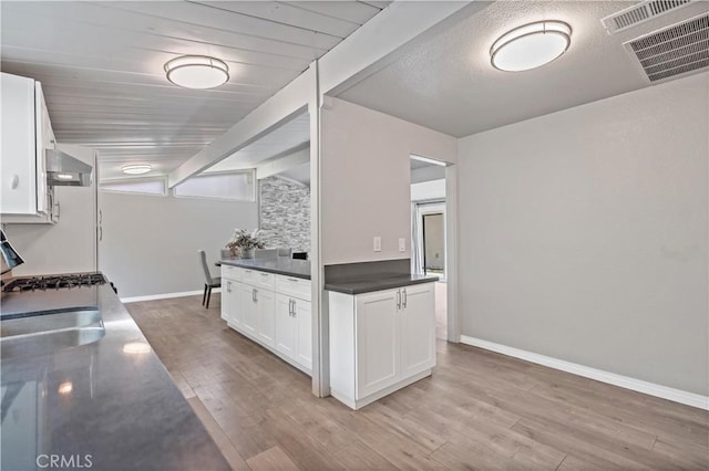 kitchen featuring visible vents, dark countertops, white cabinets, light wood-style floors, and wall chimney exhaust hood