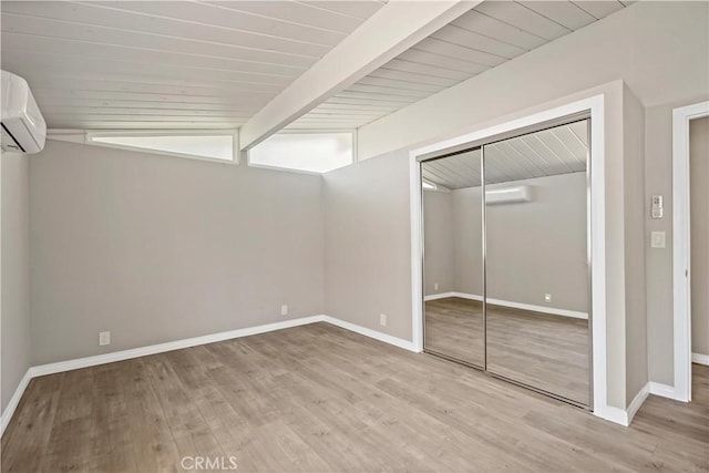 unfurnished bedroom with a closet, wood finished floors, baseboards, an AC wall unit, and a wall unit AC