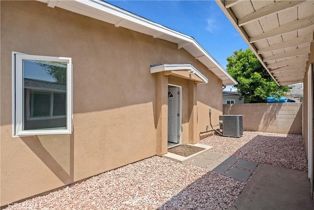 view of exterior entry featuring fence, central AC unit, and stucco siding