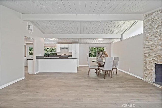 dining room featuring baseboards, vaulted ceiling with beams, light wood-style flooring, and visible vents