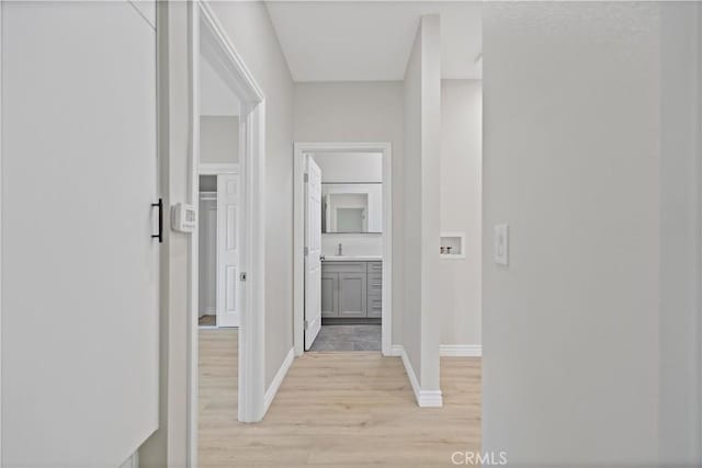corridor with light wood-style floors, baseboards, and a sink